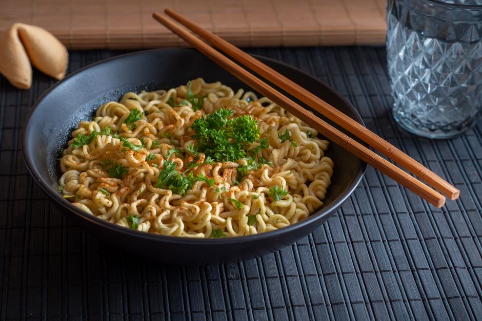 Savor a bowl of tasty noodles garnished with parsley and spring onions, ready to enjoy with chopsticks.
